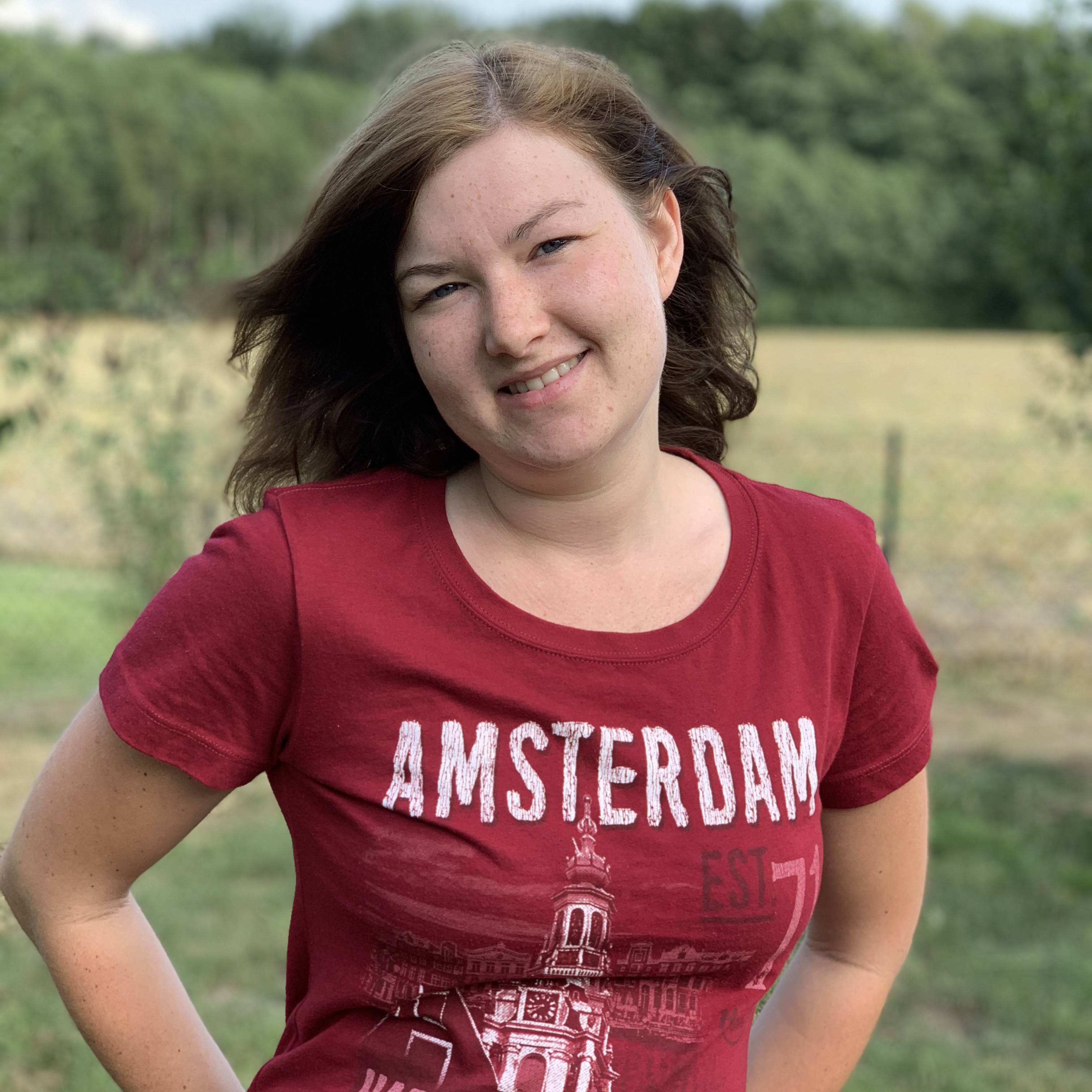 Nicole steht draußen vor einer Wiese. 